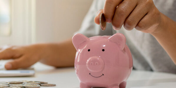 person putting money into a pink piggy bank